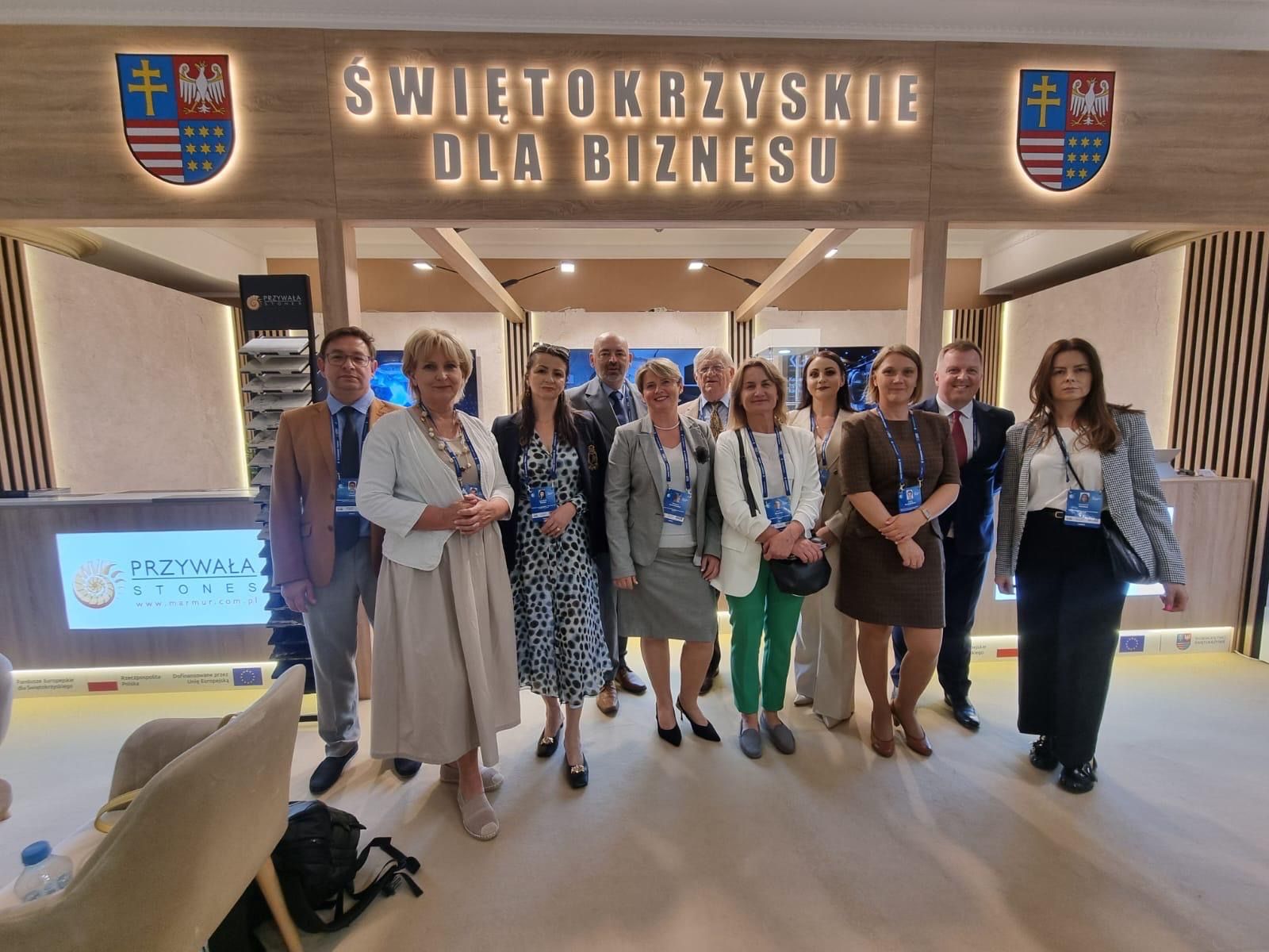 Grupa uczestników pozuje do wspólnego zdjęcia na stoisku z podświetlanym napisem „Świętokrzyskie dla biznesu”, po obu stronach herby województwa świętokrzyskiego.